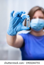 A Woman Doctor In A Mask And In Medical Gloves Shows A Medical Ampoule In Her Hand.