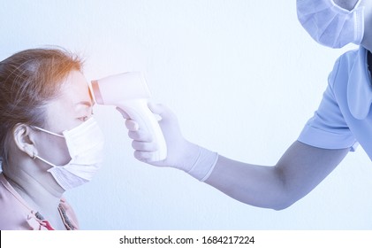 Woman Doctor Or Nurse Wear Mask And Hold Medical Device Infrared Thermometer Gun To Check Body Temperature For Coronavirus Symptoms. Initial Screening For Covid19. Coronavirus And Covid19 Concept