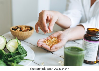 Woman doctor nutritionist hands in white shirt with omega 3, vitamin D capsules with green vegan food. The doctor prescribes a prescription for medicines and vitamins at the clinic