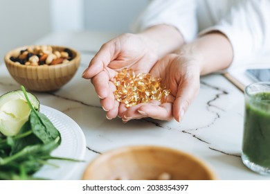 Woman doctor nutritionist hands in white shirt with omega 3, vitamin D capsules with green vegan food. The doctor prescribes a prescription for medicines and vitamins at clinic, healthy food - Shutterstock ID 2038354397