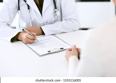 Woman doctor and patient sitting and talking at medical examination at hospital office, close-up. Therapist filling up medication history records. Medicine and healthcare concept - Powered by Shutterstock