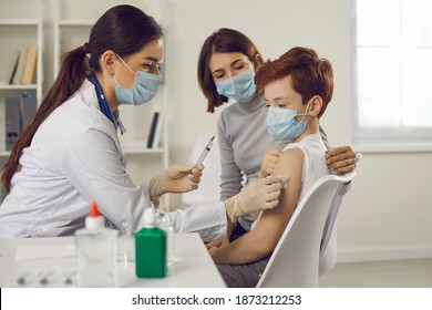 Woman Doctor Pediatrician Nurse In Medical Protective Mask Wiping Arm Of Teen Boy Patient Before Vaccination In Medical Clinic Office. Vaccination And Medicare Concept