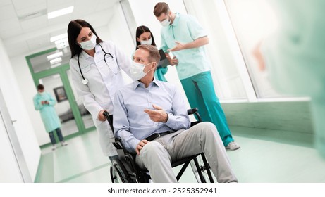 A woman doctor pushes a male patient in a wheelchair down a hospital corridor. Other medical professionals in masks work in the background. The scene shows care and communication. - Powered by Shutterstock