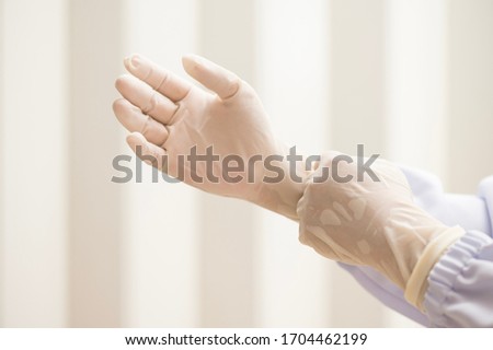Woman doctor putting white latex medical gloves on white wall background.Surgeon wearing gloves before surgery at operating room.Risk management protection health care concept.