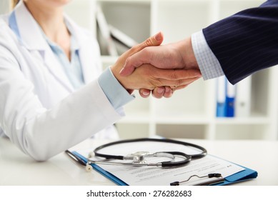 Woman doctor shaking hand with businessman in the office. Young medical specialist in uniform meeting partner for discussion. Shallow depth of field. 
