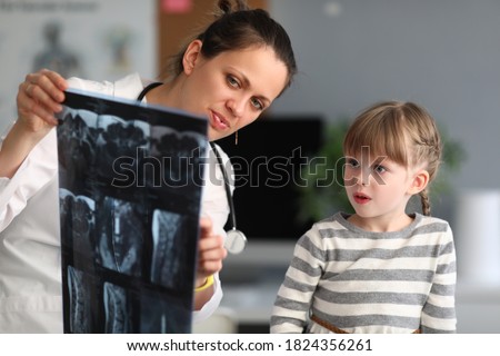Woman doctor shows child patient an xray in clinic. Use of radiation diagnostics of diseases of skeletal system in pediatric practice concept.
