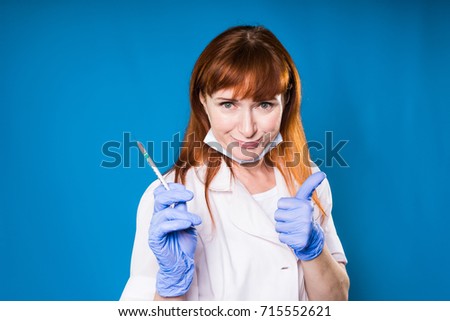 Woman doctor smiling and showing class with thumb up, holding syringe in hand.