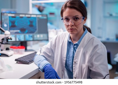 Woman Doctor Specialist In Protection Gear Looking At Camera With Safety Glasses. Researcher In Biology Medicine Lab Working With Professional Technology Equipment For Pharmaceutical Development.