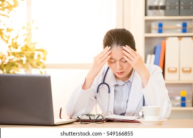 Woman Doctor Stressed With Migraine Headache Overworked. Health Care Professional In Lab Coat Wearing Stethoscope At Hospital. Mixed Race Asian Chinese Model.