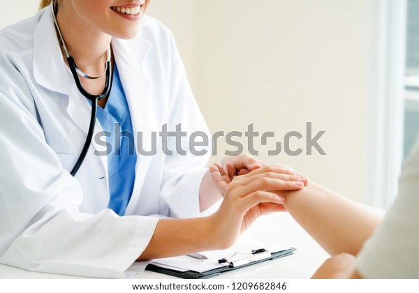 Woman doctor talks to female patient in hospital\
office while examining the patients pulse by hands. Healthcare and\
medical service.