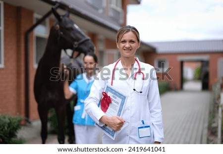 Woman doctor veterinarian holding medical certificate on background of horse. Genetic confirmation of purebred thoroughbred animals concept