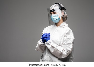 Woman doctor wearing white hazmat suit medical gloves and respirator standing isolated on gray backround quarantine crossed hands posing to camera confident
