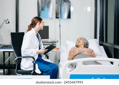 Woman doctor in white suit take notes while discussing and Asian elderly, man patient who lying on bed with receiving saline solution in hospital or clinic.
 - Powered by Shutterstock