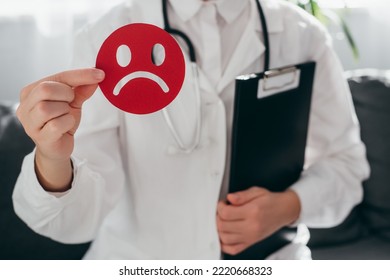 Woman doctor in white uniform with stethoscope holding little red angry emoticon and clipboard. Emotional intelligence, balance emotion control, mental health assessment, bipolar disorder concept - Shutterstock ID 2220668323