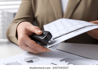 Woman with documents using stapler at white table indoors, closeup