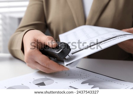 Woman with documents using stapler at white table indoors, closeup