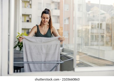 The woman does the housework. A smiling beautiful woman dressed in casual olive green clothes spreads her laundry and towel on the wire on the terrace. Arrange clean and wet laundry on the terrace