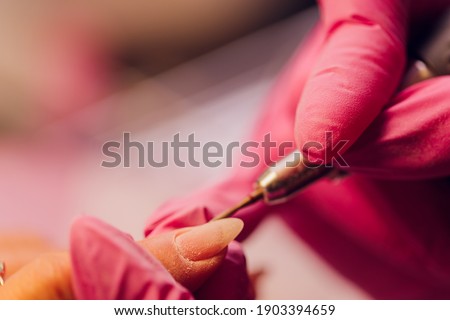 A woman does manicure with a nail device in a beauty salon, the master cuts his nails, manicures while working. Gloved hands.