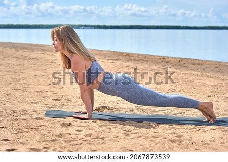 A woman does yoga on a sandy beach against the background of a river