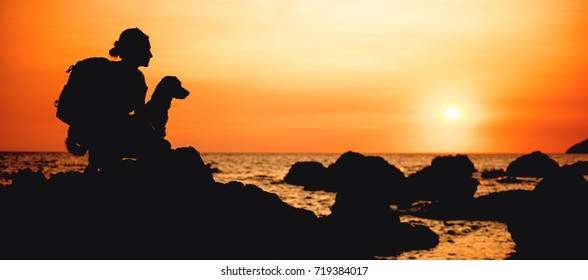 Woman with a dog hiking along the seashore during sunset