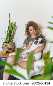 Woman Dog Lover With Bulldog At Home. Vertical View Of Woman Tickling Dog With Plants Indoors