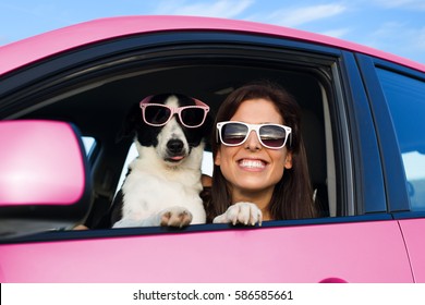 Woman And Dog In Pink Car On Summer Road Trip Vacation. Funny Dog With Sunglasses Traveling. Travel With Pet Concept.