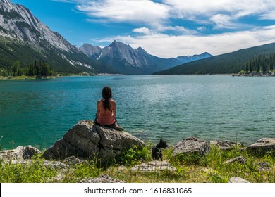 Woman With Dog Relaxing And Enjoying The View At Medicine Lake In Jasper National Park, Alberta, Canada. Accessible From Maligne Road And Formed By The Waters Of The Maligne River.