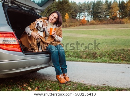 Woman with dog sit together in car trunk and warms hot tea