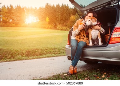 Woman With Dog Sits In Car Trunk On Autumn Road