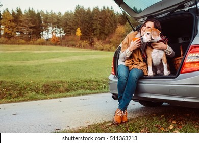 Woman With Dog Sits In Car Trunk On Autumn Road