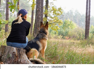 A woman with a dog are sitting on a self-isolation walk on the background of an autumn forest. View from the back. - Powered by Shutterstock