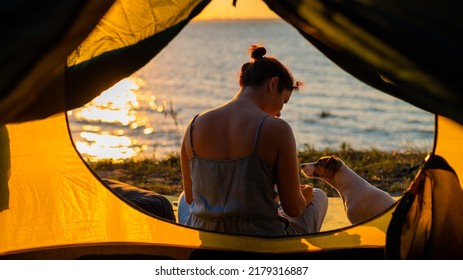 Woman and dog in a tourist tent at sunset. Camping with a pet