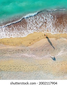 A Woman And A Dog Walking Along The Sea Shore Leaving Footprints On Sand, Aerial Vertical Shot Directly Above