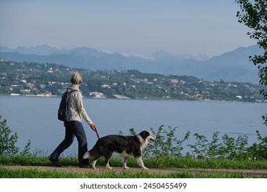 Woman with a dog walking in motion in the background Lake Garda, mountain peaks in the snow. - Powered by Shutterstock