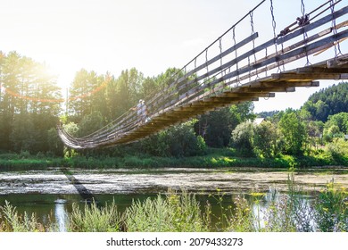 Woman with dog walks along old wooden hanging bridge on river in summer sunny day. Natural landscape. Dog on bridge.