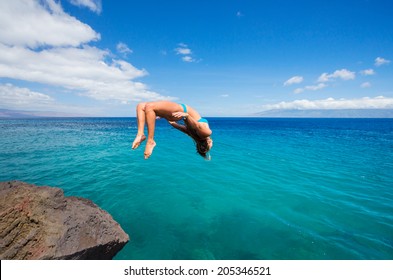 Woman doing backflip off cliff into the ocean. Summer fun lifestyle.