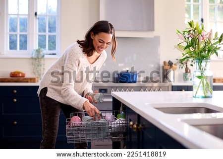 Woman Doing Chores Loading Dishwasher In Kitchen At Home