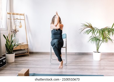 Woman doing Eagle pose on chair - Powered by Shutterstock