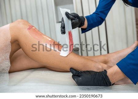 Woman doing epilation shugaring with hot pasta removing unwanted hair on legs. Depilation wax.  The concept of grooming the body. Cosmetic application foot zone.
