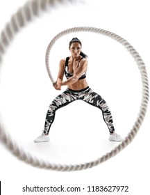 Woman doing exercises with battle rope. Photo of muscular model in military sportswear isolated on white background. Strength and motivation