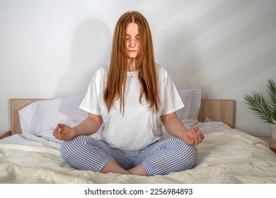 Woman doing exercises in bed at home in the morning. Sukhasana yoga pose open mind. Lady with long hair in pajamas. Girl on clean white bedding with cozy blanket. Healthy lifestyle, balance, wellness