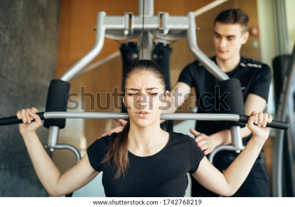 Woman doing fitness exercises on home gym lat\
pull down machine with personal trainer.Making an effort and\
training hard for fit body.Excess body weight.Home weight\
workout.Dedication and\
motivation