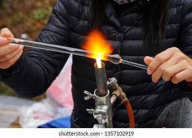 A Woman Is Doing A Glassblowing On A Long Glass Rod.