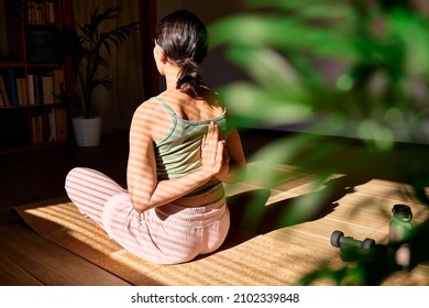 Woman doing Gomukhasana or Cow Face Pose sitting in lotus pose on yoga mat. Wellbeing. Mindful meditation concept. Wellbeing. Practicing yoga at home.