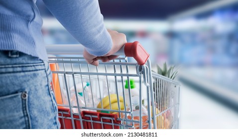 Woman doing grocery shopping at the supermarket, she is pushing a shopping cart, hand close up