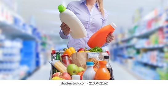 Woman doing grocery shopping at the supermarket and comparing products, she is checking two bottles of laundry detergent