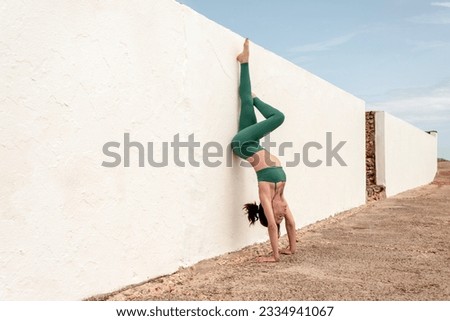 woman doing a handstand against a white wall, outdoor exercise.