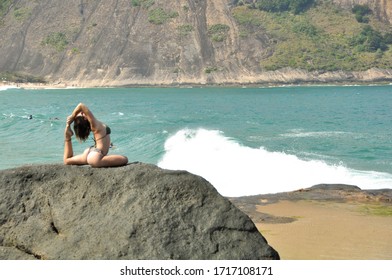 A Woman Doing A Hard Yoga Pose Wich Requires Skills And Elasticity. She Is Stretching On Top A Big Rock Under The Sun At At Beach.