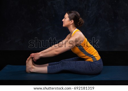 Woman doing Hatha yoga Ashtanga Vinyasa yoga asana Paschimottanasana - seated forward bend beginner variation on dark grunge background