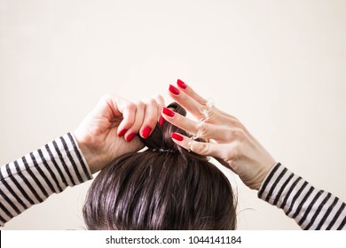 woman is doing her hair, straightened, combing, the disheveled bun on her head.  Dark hair is tied with a transparent spiral elastic band. Modern fast hairstyle. Cares about a beautiful hair. Copyspac